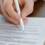 Persona firmando un contrato de relevo con bolígrafo blanco.