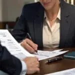 Profesional firma documentos de compraventa ante un escritorio.