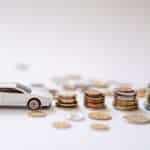 Coche de juguete junto a monedas apiladas y dinero en efectivo.
